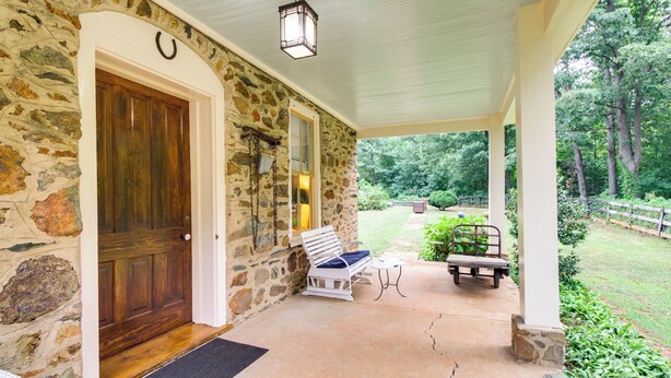 A stone house with a wooden door, a porch with a bench, and a garden view. - Monticello Wine Trail Cottage - Close to Hiking! (Afton)
