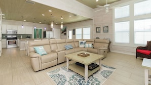A spacious living area with a large L-shaped beige sofa, a coffee table, and a kitchen in the background. - Pet Friendly Shared Pool Sleeps 14 (Port Aransas)