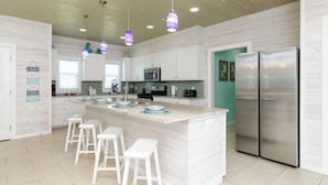 A modern kitchen with white cabinetry, a central island with bar stools, stainless steel appliances, and pendant lighting. - Pet Friendly Shared Pool Sleeps 14 (Port Aransas)