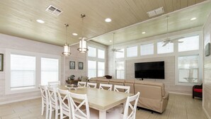 A spacious living area with a large sofa, a dining table with chairs, and a flat-screen TV mounted on the wall. - Pet Friendly Shared Pool Sleeps 14 (Port Aransas)