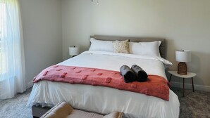 Una cama bien tendida con ropa de cama blanca y roja, un ventilador de techo y dos lámparas de noche.