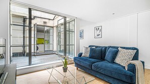 A modern living room with a blue sofa, a glass coffee table, and a potted plant.