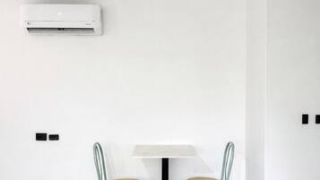 A room with a white air conditioning unit, a small table with two chairs, and a red object on the floor.