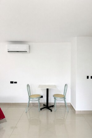 A room with a white air conditioning unit, a small table with two chairs, and a red object on the floor. - Hotel Ofix - Laureles (Medellín)