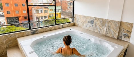 A person in a hot tub with a view of buildings outside.
