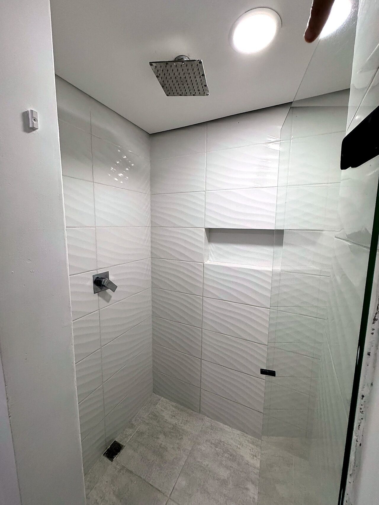 A small, enclosed shower area with white tiles and a single overhead light.