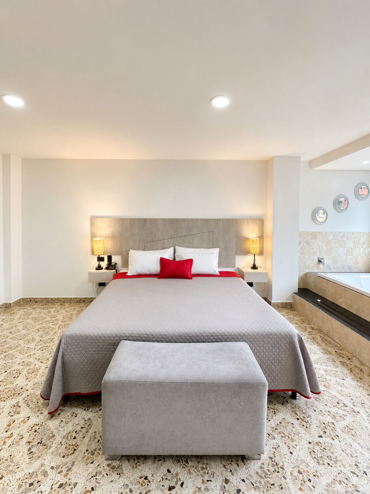 Una camera d'albergo moderna con un letto grande, un angolo salotto, un bagno con vasca e una TV a parete.