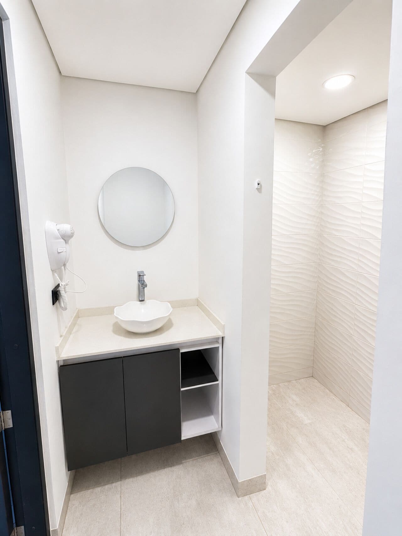 Ein modernes Badezimmer mit einem weißen Waschbecken, einem runden Spiegel und einem Handtuchspender.