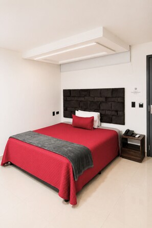 A modern bedroom with a large bed, a headboard, a bedside table with a phone, and a door. - Hotel Ofix - Laureles (Medellín)