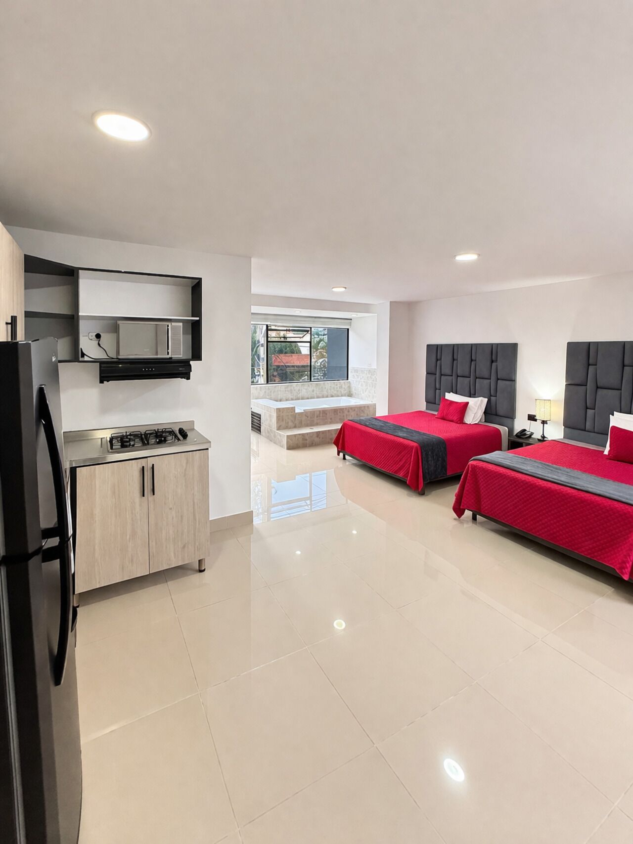 Habitación de hotel moderna con kitchenette, dos camas, baño y vistas al exterior.