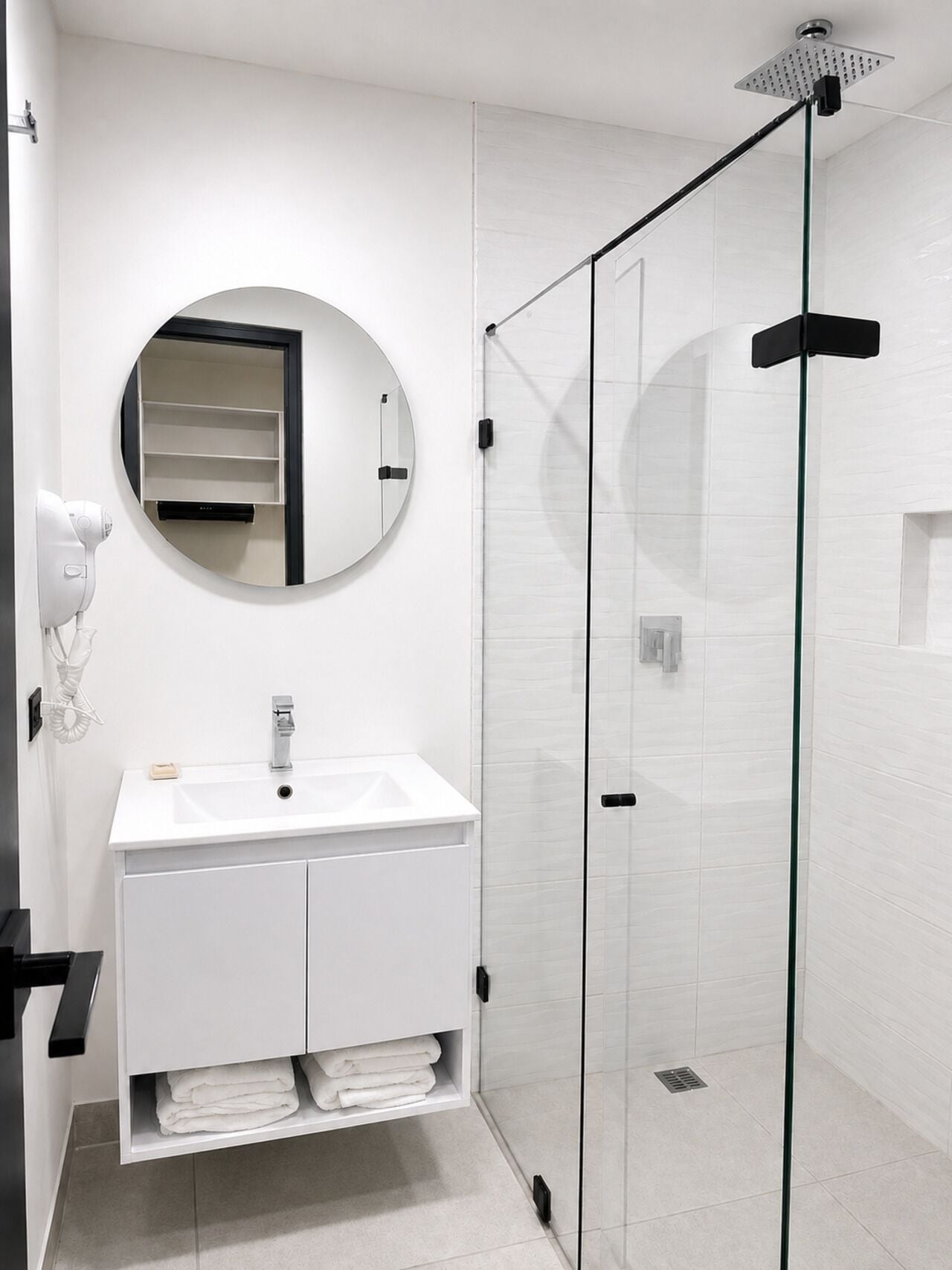 A modern bathroom with a white vanity, a round mirror, and a glass-enclosed shower.