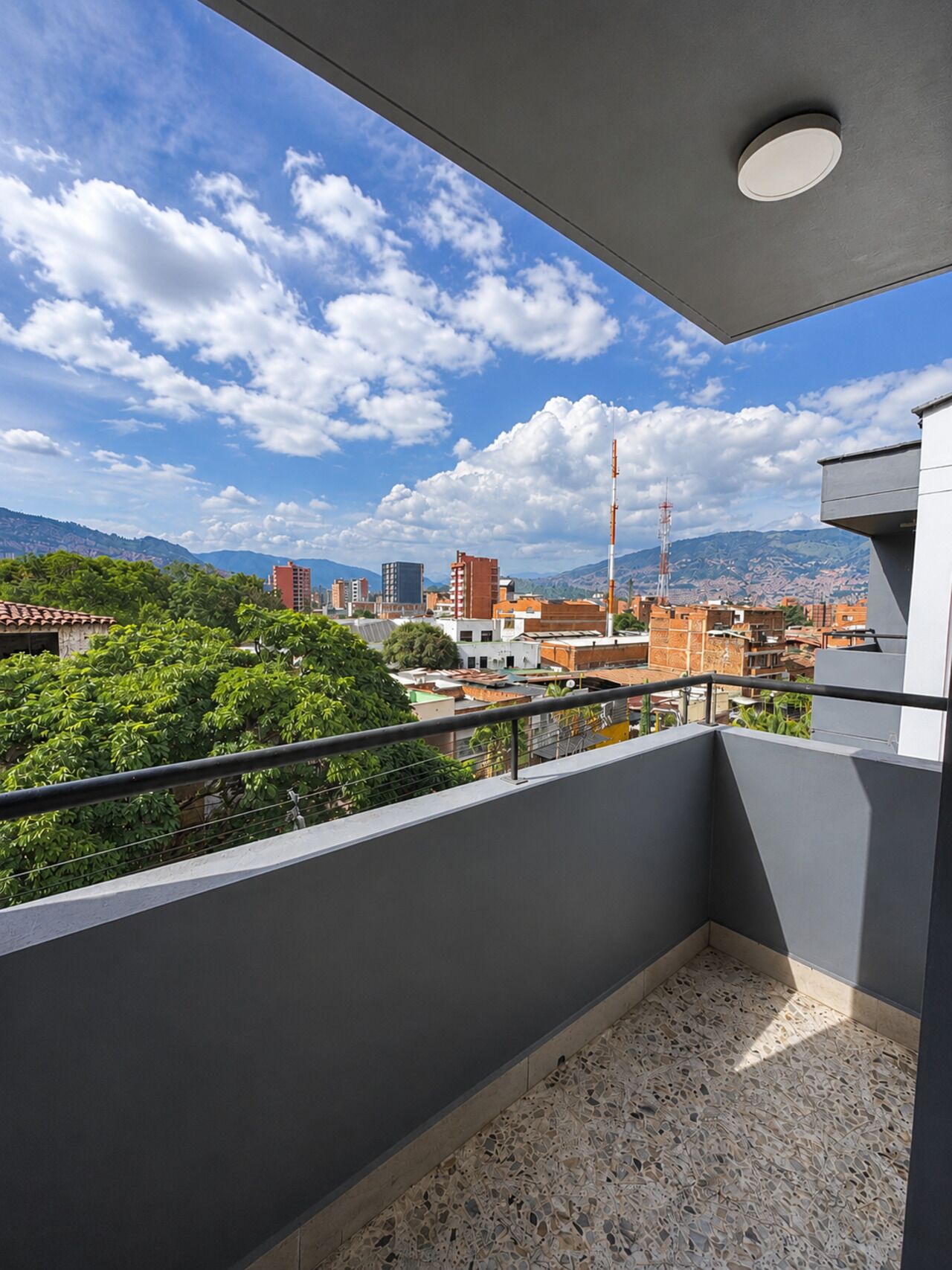 A balcony with a view of a cityscape, including buildings and mountains.
