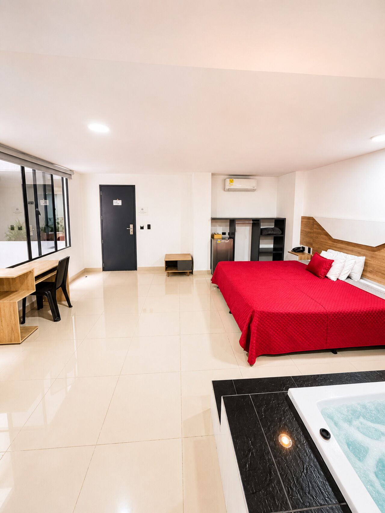 A hotel room with a bed, a desk, a small kitchenette, and a bathroom with a bathtub.
