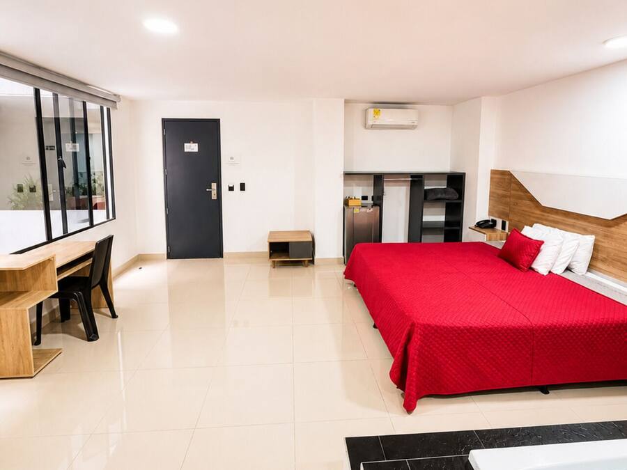 Een hotelkamer met een bed, een bureau, een kleine kitchenette en een badkamer met een bad.