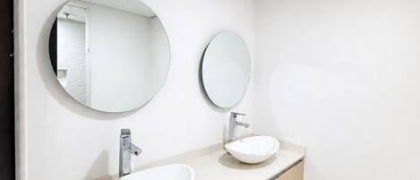 A modern bathroom with two sinks, a mirror, and a light fixture.