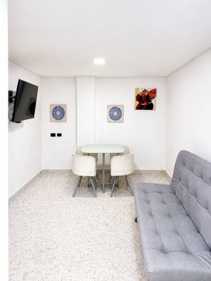 A room with a round table, two chairs, a grey sofa, a flat-screen TV mounted on the wall, and two framed artworks. - Hotel Ofix - Laureles (Medellín)