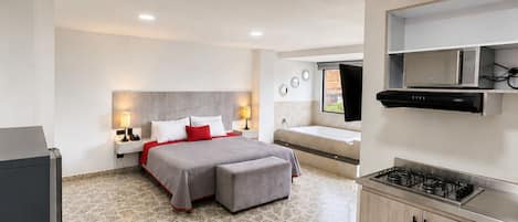 A modern hotel room with a bed, a small kitchenette, a bathroom, and a large window.
