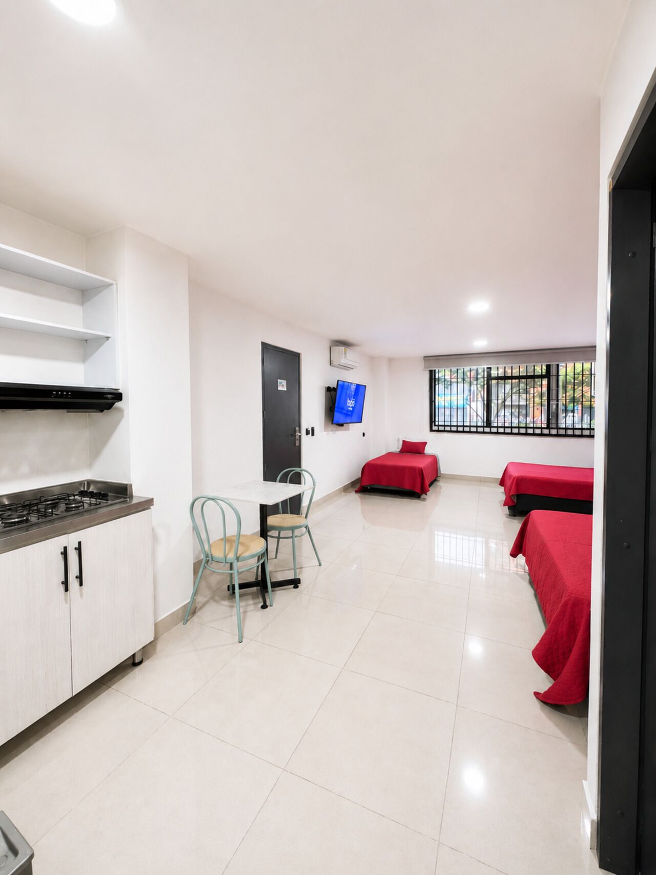 Una camera d'albergo con angolo cottura, zona pranzo con una sedia e un letto con copripiumino rosso.