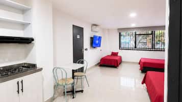 Une chambre d’hôtel avec une kitchenette, un coin repas comprenant une chaise et un lit recouvert d’une couverture rouge.