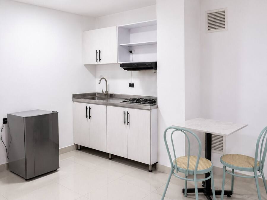 Une cuisine compacte avec des meubles blancs, une cuisinière à gaz, un évier et une petite table à manger avec deux chaises.