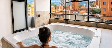 Una mujer se relaja en un jacuzzi con vistas a la ciudad a través de amplias ventanas.