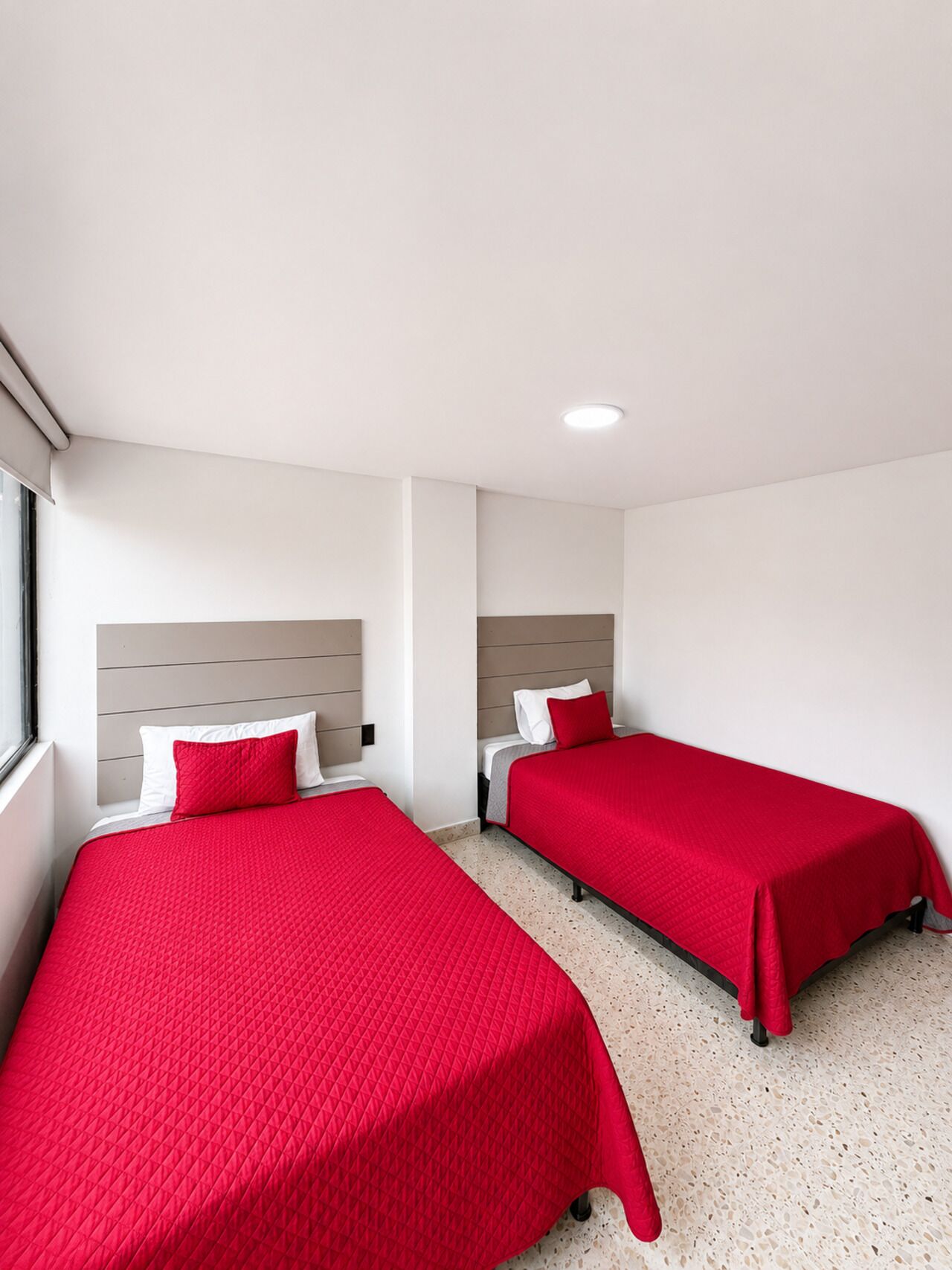 Habitación de hotel con dos camas, cada una con colcha roja y almohadas blancas.
