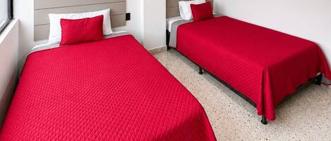 Habitación de hotel con dos camas, cada una con colcha roja y almohadas blancas.
