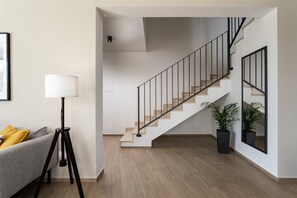 A modern interior with a staircase, a sofa, a floor lamp, and two potted plants.