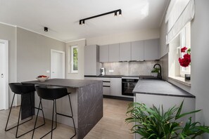 A modern kitchen with a central island, bar stools, a built-in oven, and a window with red flowers.