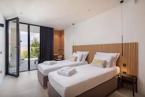 Une chambre d’hôtel moderne avec deux lits, une porte-fen être coulissante donnant sur un balcon et une petite table avec une chaise.