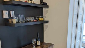 A room with a dark wall, a wooden table with a wine bottle, and shelves with books and decorative items.