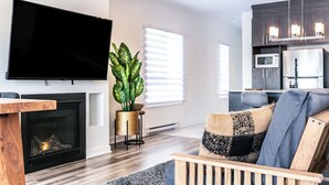 A modern living room with a flat-screen TV, a fireplace, a large potted plant, and a cozy seating area.