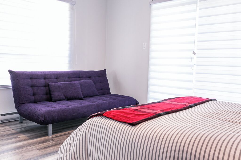 A modern bedroom with a bed, a purple sofa, and a window with blinds.