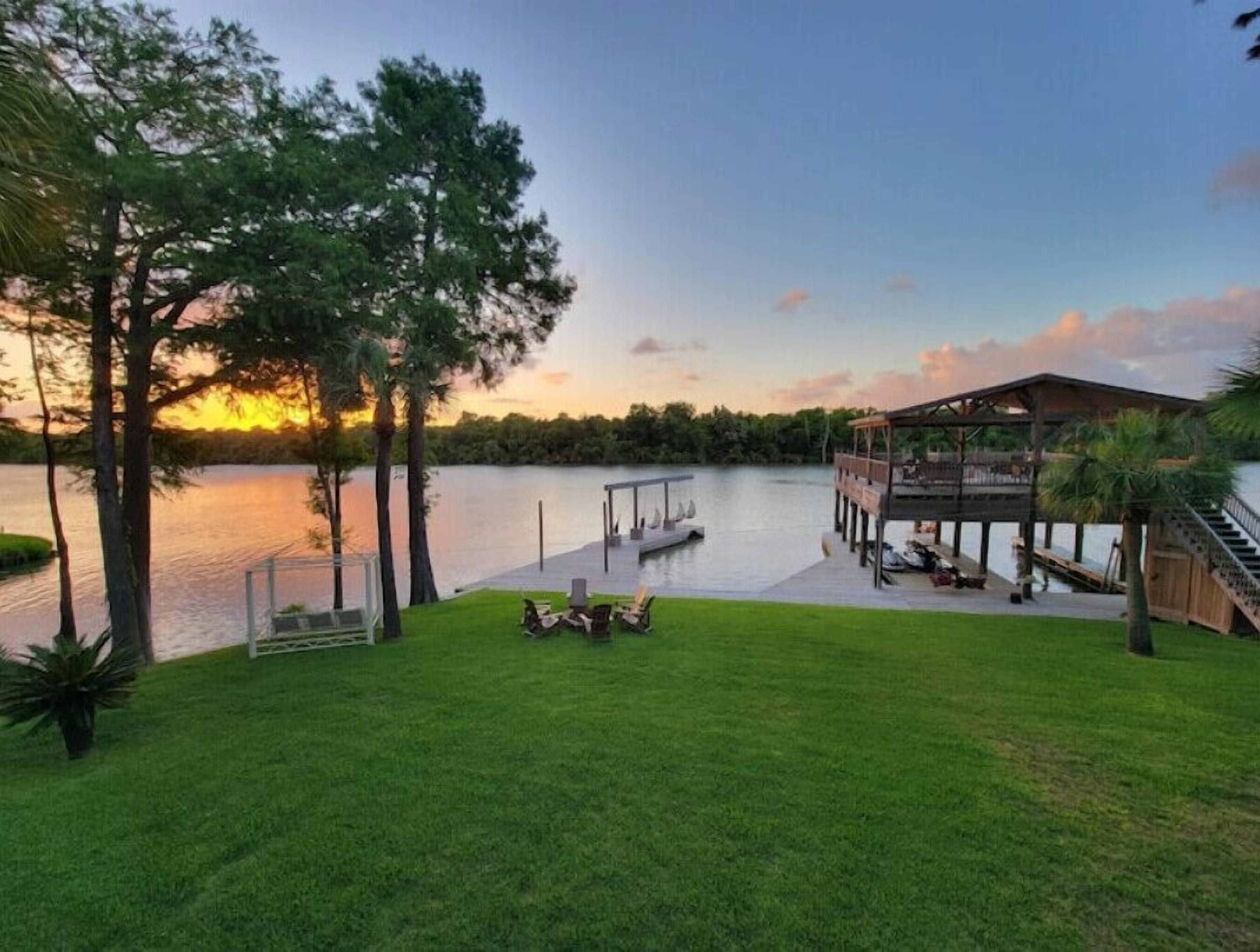 Une propriété au bord du lac, dotée d’une pelouse verdoyante, d’une terrasse en bois et d’un belvédère offrant une vue sur l’eau.