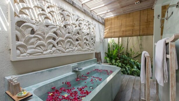 Ein Wellnessbereich mit einer großen Badewanne, gefüllt mit Rosenblättern, einer Holzbank und einer Wand mit aufwendigen Schnitzereien.