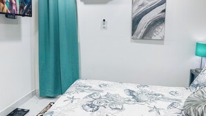 Ett sovrum med en säng, turkosa gardiner, en luftkonditioneringsanläggning, en väggmonterad ljusströmbrytare och en tavla.
