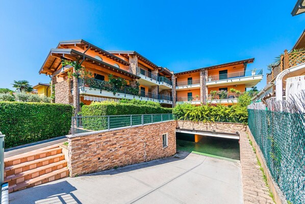 A multi-story residential building with balconies, a stone wall, and a small bridge. - Annamaria 9 con Piscina by Wonderful Italy (Sirmione)