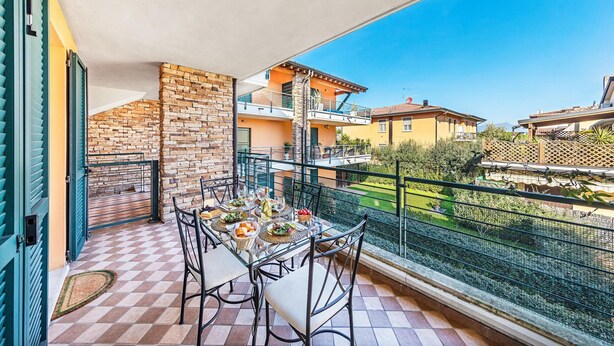 A balcony with a table set for dining, a stone wall, and a view of neighboring buildings. - Annamaria 9 con Piscina by Wonderful Italy (Sirmione)