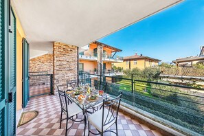 A balcony with a table set for dining, a stone wall, and a view of neighboring buildings. - Annamaria 9 con Piscina by Wonderful Italy (Sirmione)