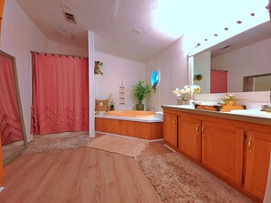 Un baño con tocador de madera, bañera, espejo grande y cortina de ducha.
