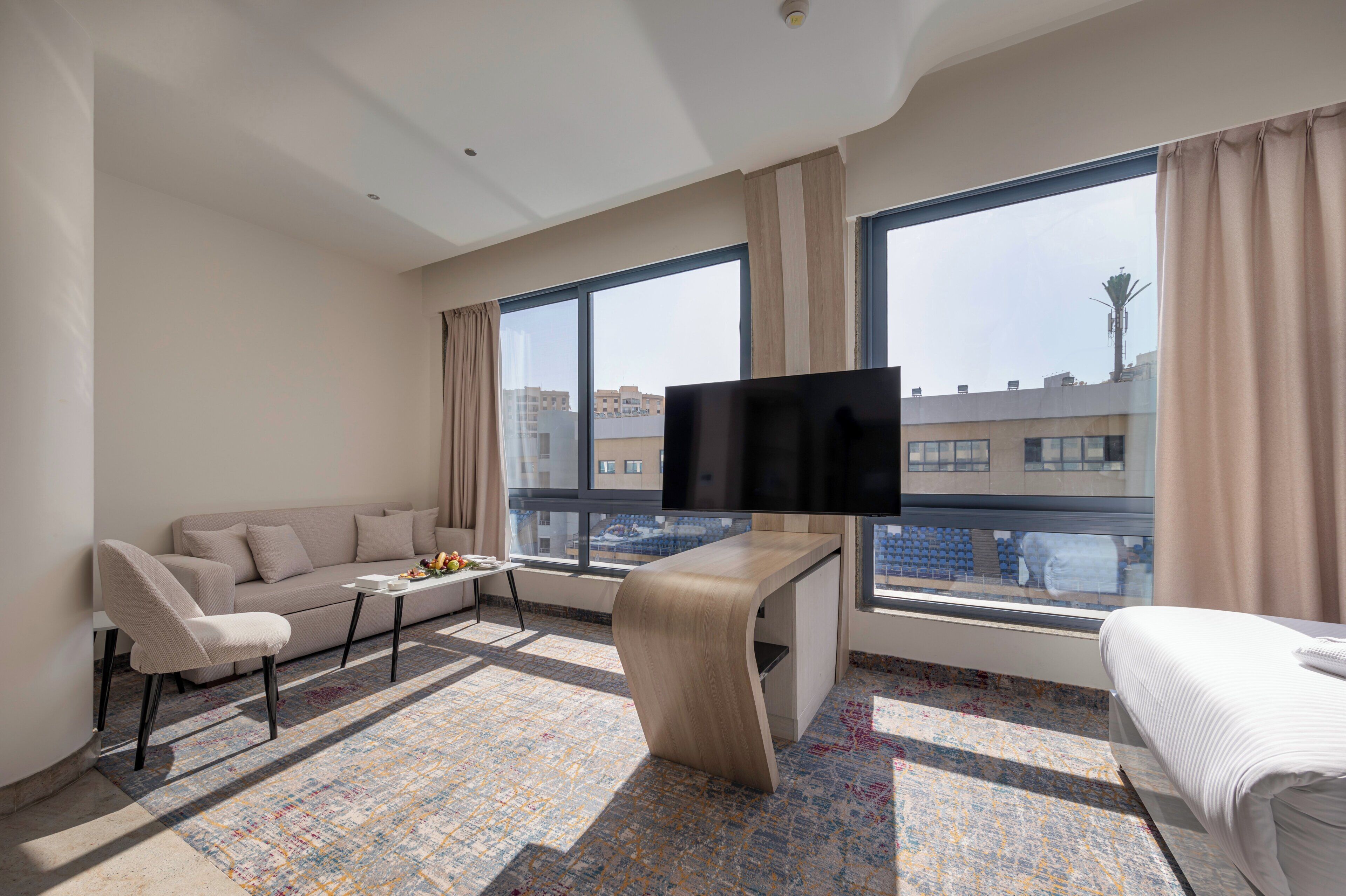 Une chambre d’hôtel moderne avec un canapé, un téléviseur fixé au mur, une petite table et un lit.