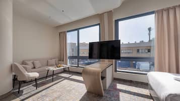 Une chambre d’hôtel moderne avec un canapé, un téléviseur fixé au mur, une petite table et un lit.