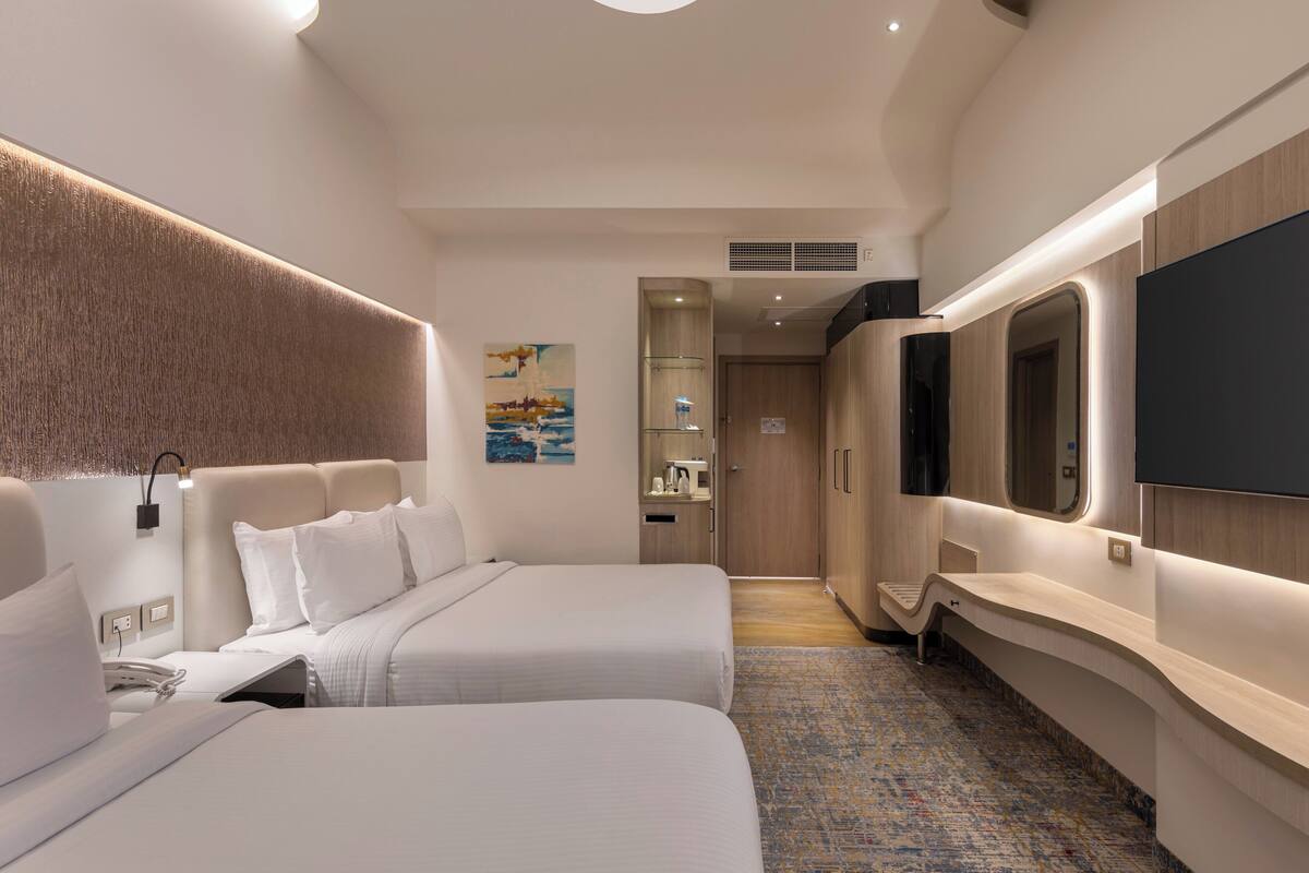 Ein modernes Hotelzimmer mit zwei Betten, einem Flachbildfernseher, einem großen Spiegel und einem Gemälde an der Wand.