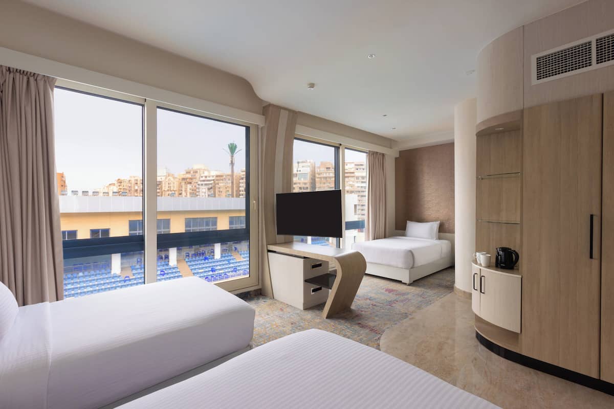 A hotel room with a large window, a bed, a desk with a TV, and a wardrobe.
