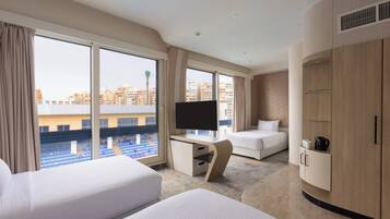 Habitación de hotel con un ventanal grande, una cama, un escritorio con televisor y un armario.