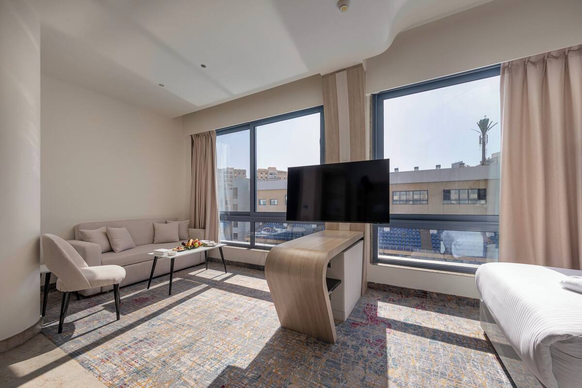 Ein modernes Hotelzimmer mit einer Couch, einem Wandfernseher, einem kleinen Tisch und einem Bett.