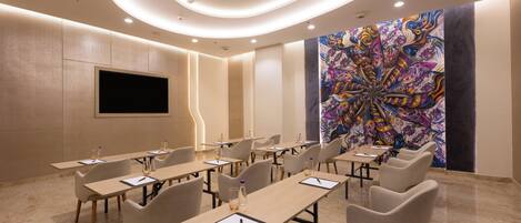 A conference room with multiple tables and chairs, a flat-screen TV mounted on the wall, and a colorful abstract painting on the wall.