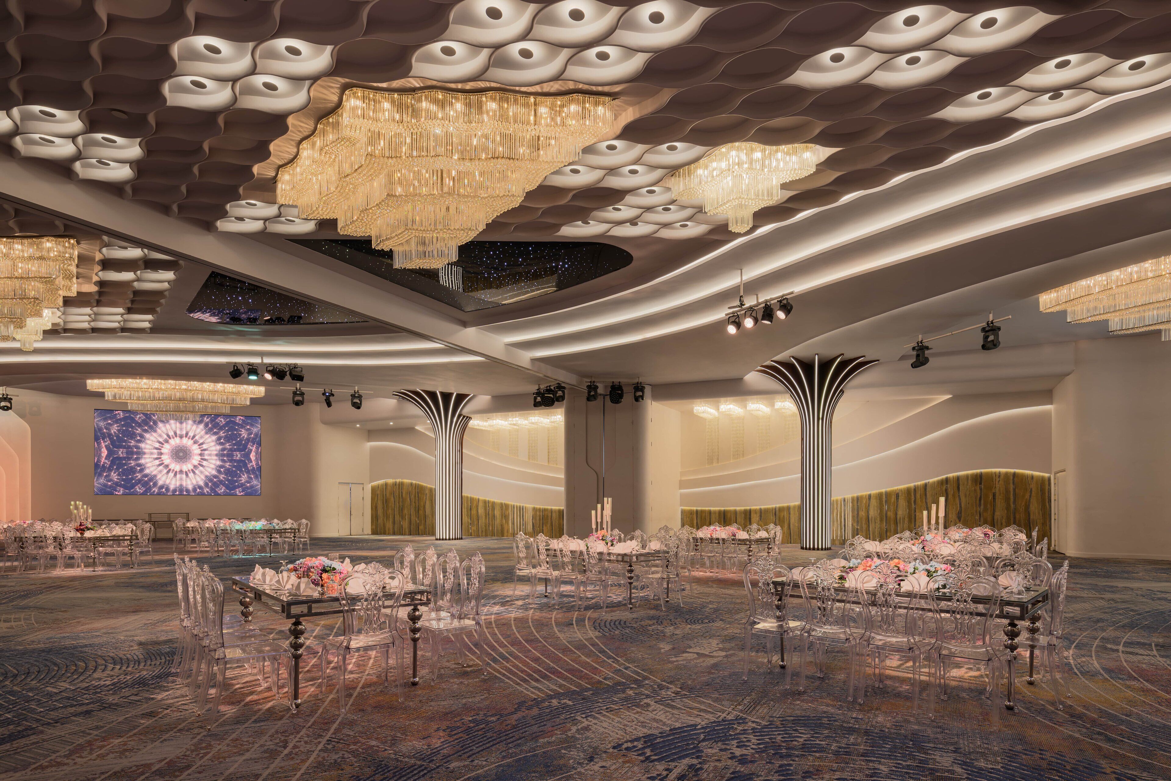 Un amplio salón de banquetes con asientos escalonados, candelabros y una gran pantalla digital.