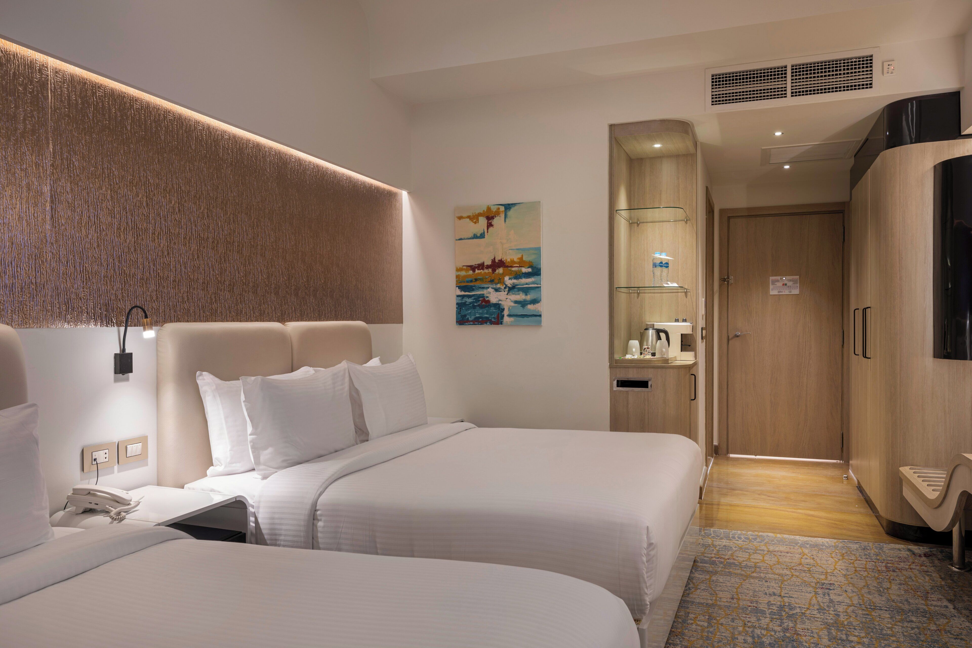 Habitación de hotel con dos camas, un televisor montado, un cuadro en la pared y un armario de madera.