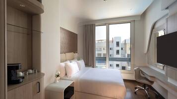 A modern hotel room with a bed, a desk, a chair, a TV, and a window with a city view.